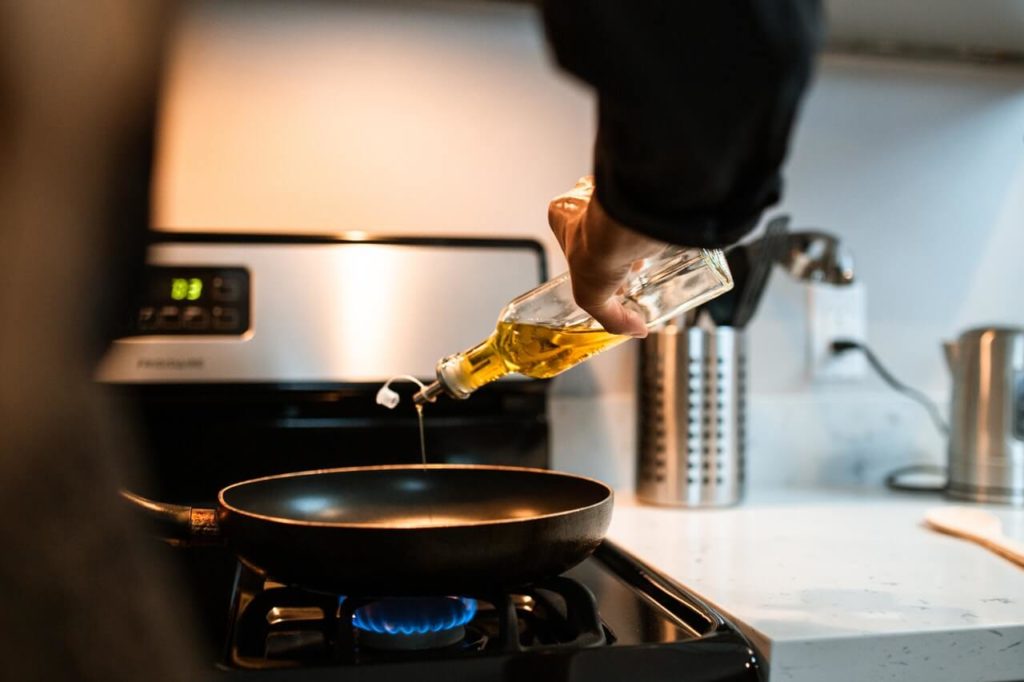 Photo d'une personne versant de l'huile dans une poêle pour illustrer la cuisson de la viande en poudre