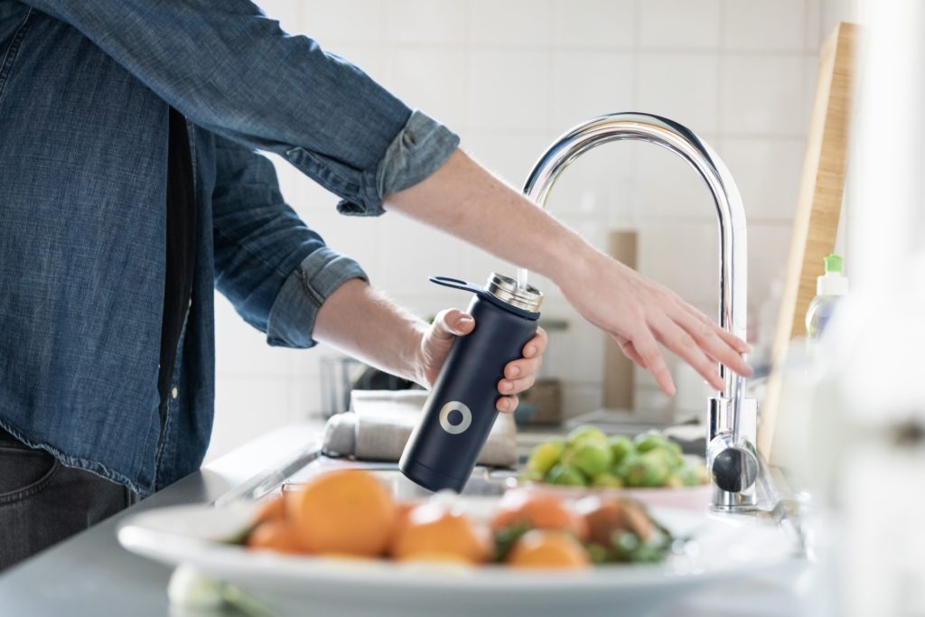 Personne remplissant une gourde métallique au robinet, lui permettant de réduire ses déchets ménagers en évitant l'achat d'une bouteille d'eau