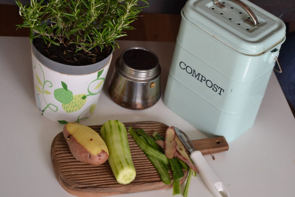 Épluchures de légumes sur une planche à découper, une plante et un petit bac à compost permettant de réduire ses déchets ménagers