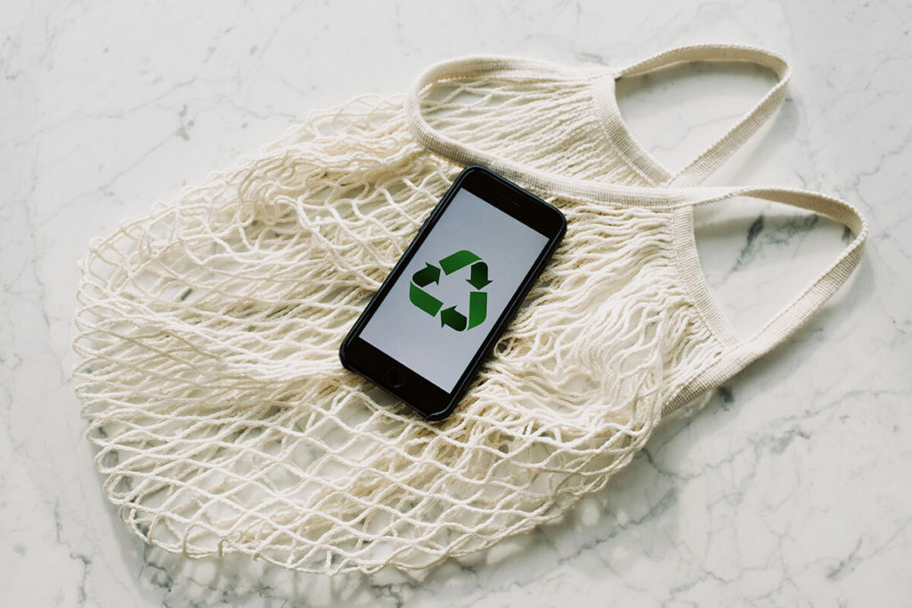 Sac écologique avec par dessus un smartphone avec le logo de recyclage, pour montrer le greenwashing à travers les étiquetages mensongers
